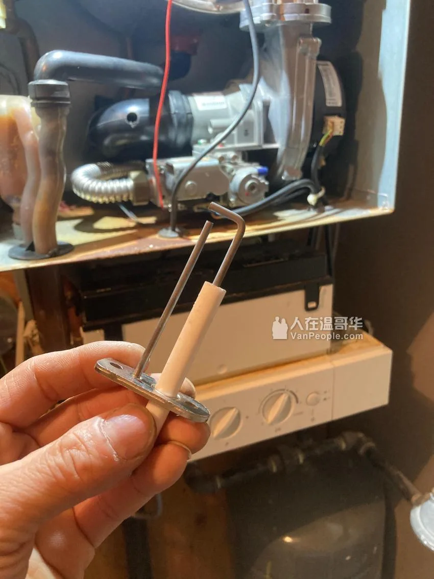 手里拿着刚从暖炉上拆下来的火焰感应针，后面机器开着，控制面板露在外面。