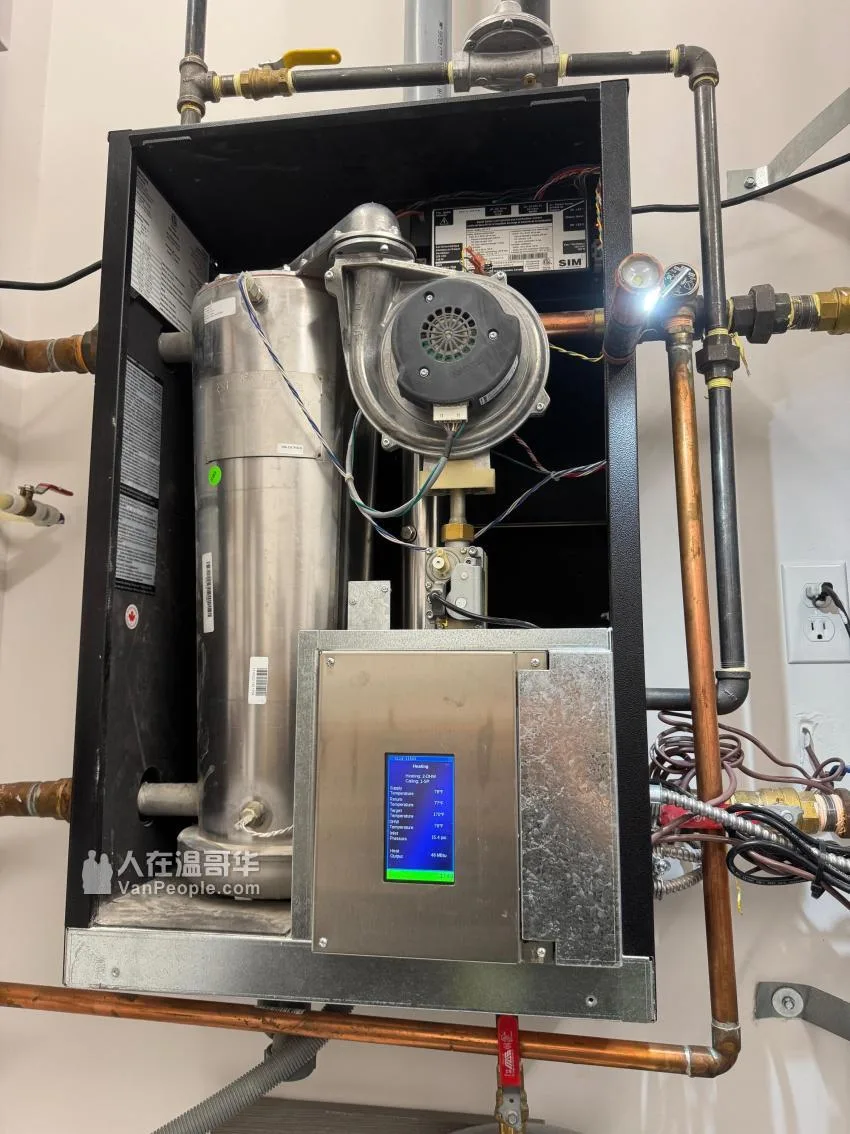 A boiler cabinet open under a work light, its inducer blower and control display visible with the system running.